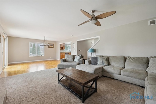 living room with light wood-style floors, visible vents, baseboards, and ceiling fan with notable chandelier