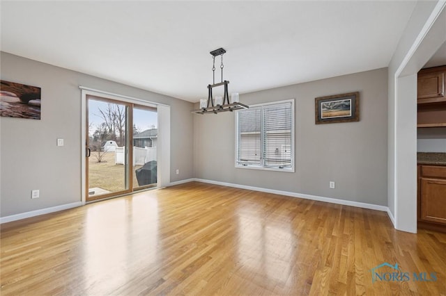 unfurnished dining area with light wood-type flooring, an inviting chandelier, and baseboards