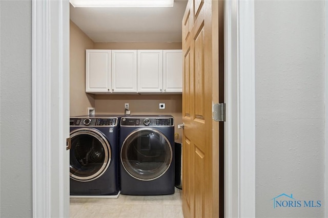 clothes washing area with cabinet space, light floors, and washing machine and clothes dryer