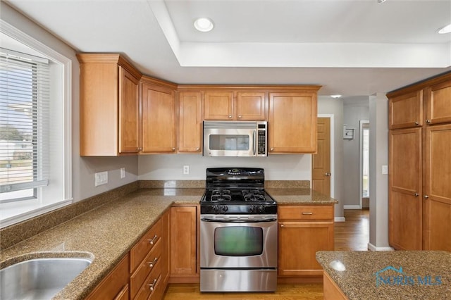 kitchen featuring appliances with stainless steel finishes, brown cabinetry, light wood finished floors, and dark stone countertops