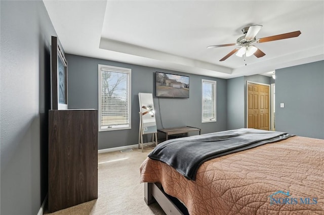 bedroom featuring a tray ceiling, a closet, light carpet, ceiling fan, and baseboards