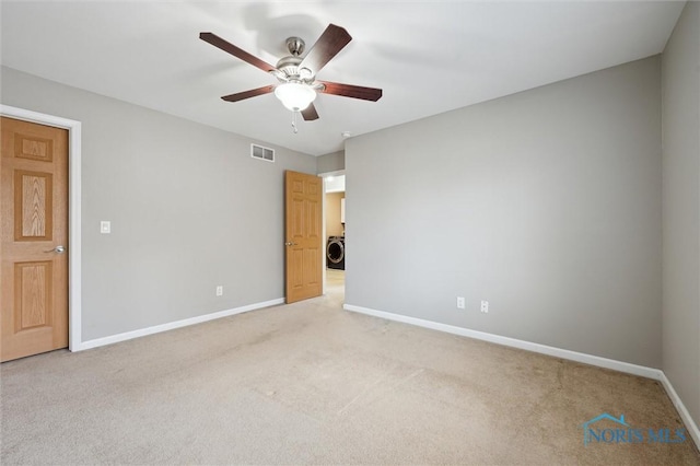 spare room featuring light carpet, baseboards, visible vents, a ceiling fan, and washer / clothes dryer