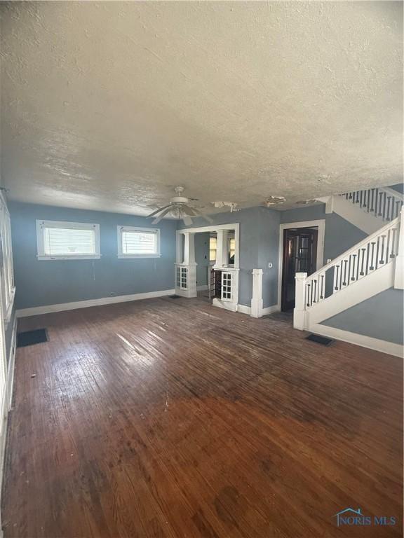 unfurnished living room with wood-type flooring, stairs, baseboards, and a textured ceiling