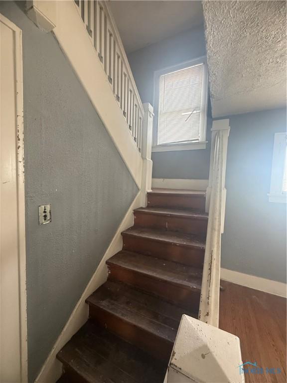 stairs with a textured ceiling, wood finished floors, and baseboards