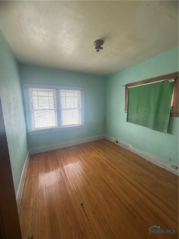 spare room featuring wood-type flooring and baseboards