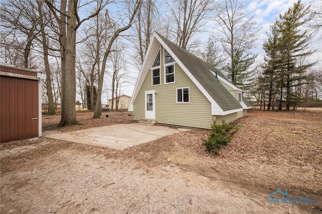 rear view of house featuring entry steps, driveway, and a shingled roof