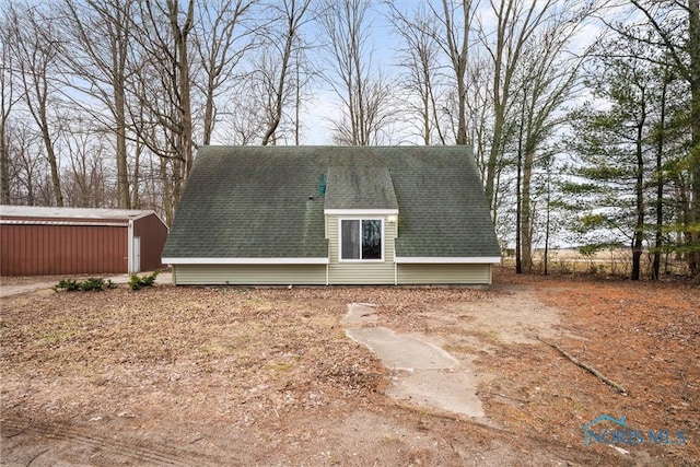 rear view of house with a shingled roof and an outdoor structure