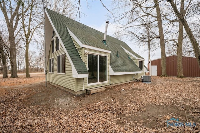 back of house with a garage, central AC, and a shingled roof