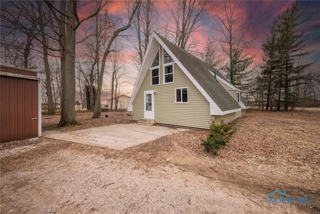 rear view of house featuring entry steps, dirt driveway, and roof with shingles