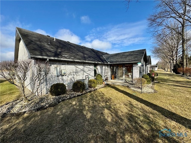 back of property featuring a yard, a shingled roof, and brick siding