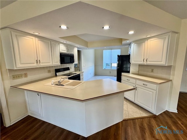 kitchen with wood finished floors, a sink, white cabinetry, black appliances, and a tray ceiling