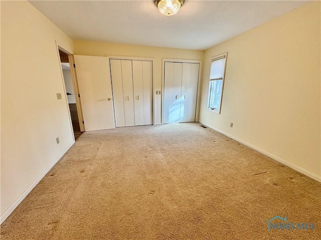 unfurnished bedroom with multiple closets, carpet floors, baseboards, and a textured ceiling