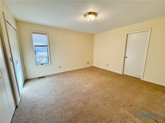 unfurnished bedroom featuring a textured ceiling, carpet flooring, visible vents, and baseboards