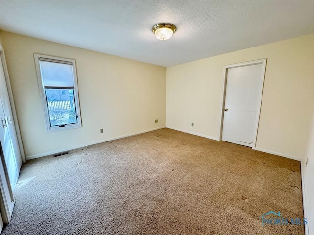 spare room with carpet floors, visible vents, a textured ceiling, and baseboards