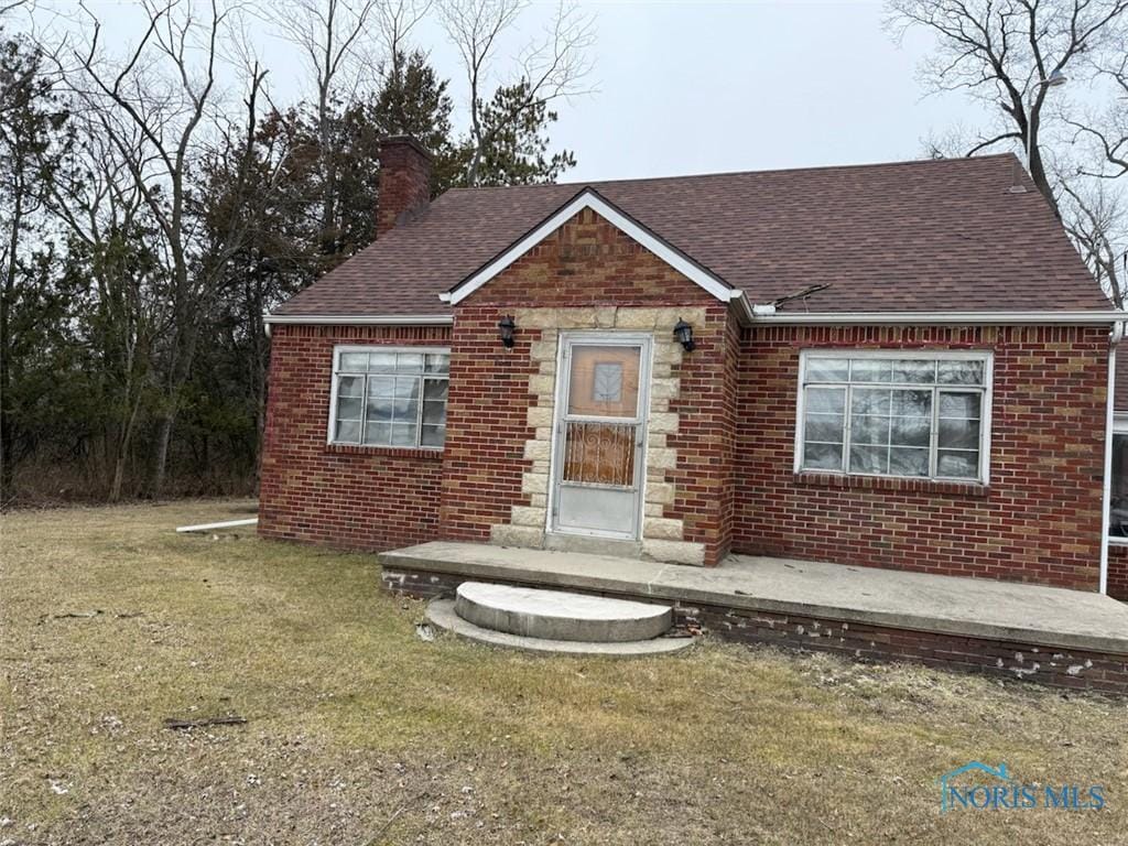 bungalow-style home with brick siding, a shingled roof, stone siding, a chimney, and a front yard