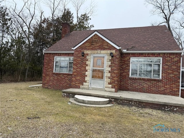 bungalow-style home featuring brick siding, a shingled roof, a front lawn, a chimney, and stone siding