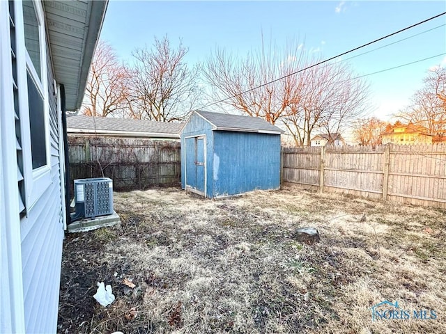 view of yard with central air condition unit, a fenced backyard, an outdoor structure, and a shed