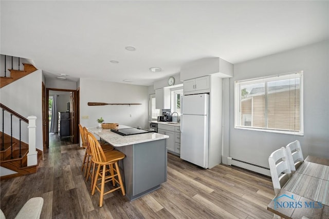 kitchen featuring a baseboard radiator, a kitchen breakfast bar, wood finished floors, freestanding refrigerator, and a sink