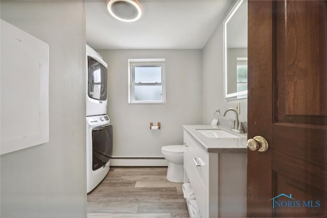 bathroom with toilet, baseboard heating, stacked washer / dryer, vanity, and wood finished floors