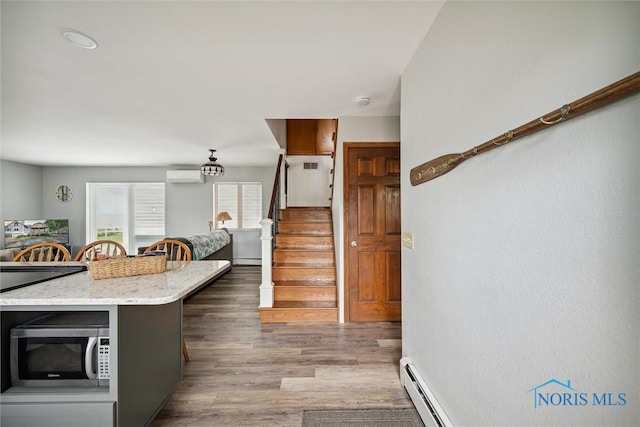 kitchen with baseboard heating, stainless steel microwave, a wall mounted air conditioner, and wood finished floors