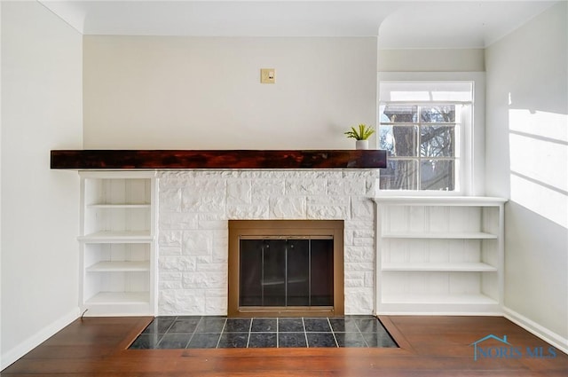 room details featuring a stone fireplace, baseboards, wood finished floors, and built in features