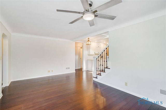 spare room featuring baseboards, stairway, arched walkways, a ceiling fan, and dark wood finished floors