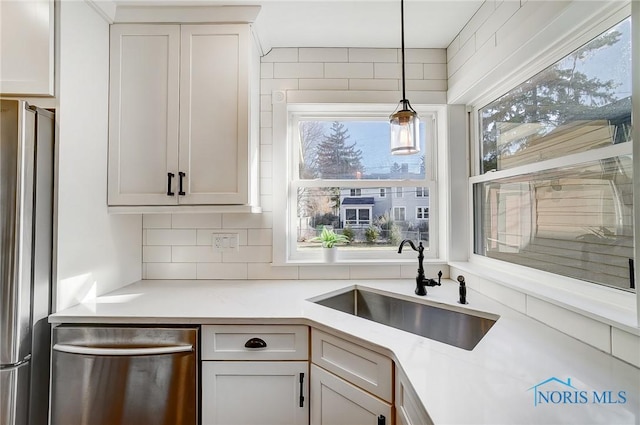 kitchen featuring hanging light fixtures, a sink, light countertops, stainless steel appliances, and backsplash