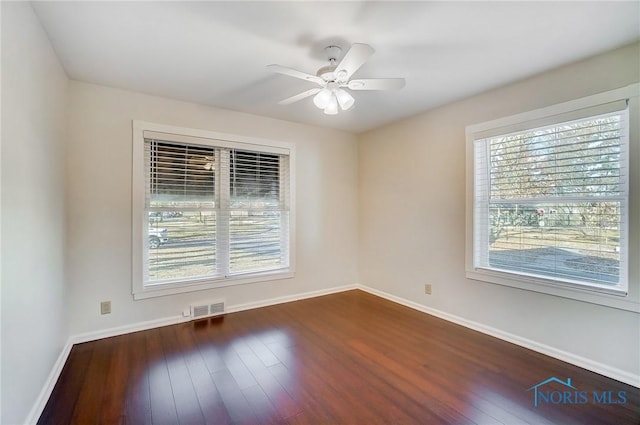 empty room featuring visible vents, baseboards, dark wood-style flooring, and ceiling fan