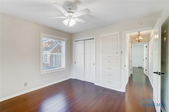 unfurnished bedroom with dark wood-type flooring, baseboards, ceiling fan with notable chandelier, and a closet