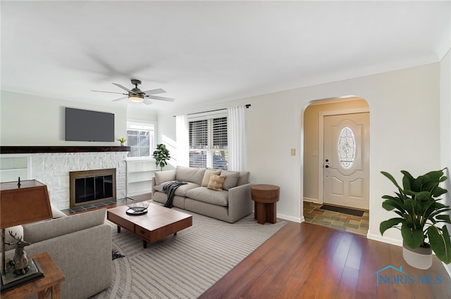 living area featuring arched walkways, ceiling fan, a healthy amount of sunlight, and hardwood / wood-style flooring