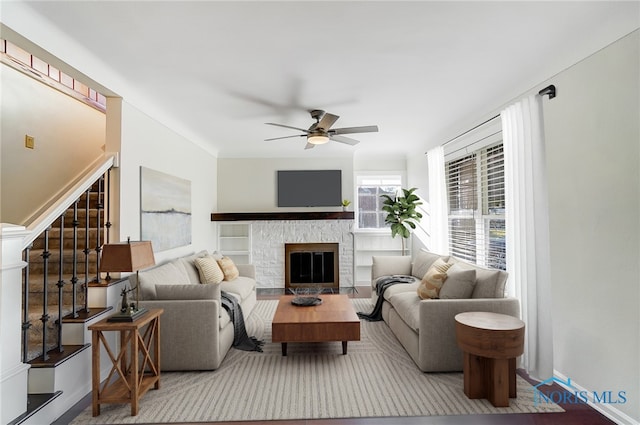 living area featuring a ceiling fan, baseboards, stairway, and a fireplace
