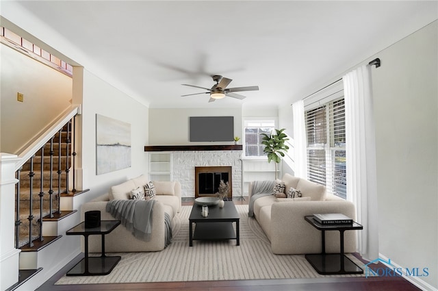living area featuring stairs, a ceiling fan, baseboards, and a fireplace