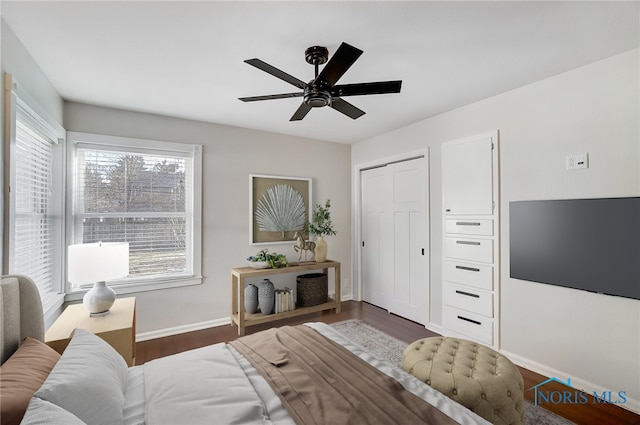 bedroom with dark wood-style flooring, baseboards, a ceiling fan, and a closet