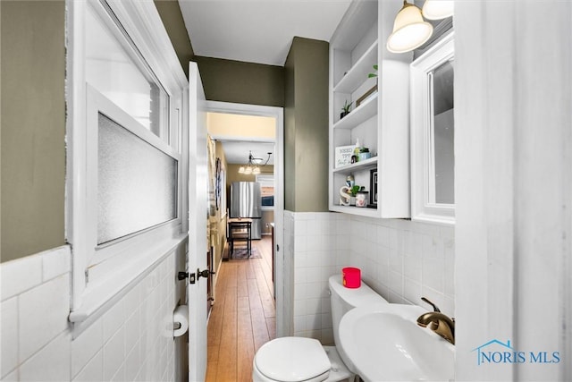 bathroom featuring toilet, wood finished floors, a sink, tile walls, and wainscoting