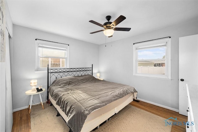 bedroom with ceiling fan, multiple windows, baseboards, and wood finished floors