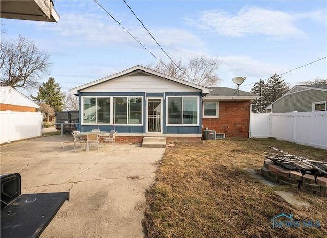 back of house with brick siding, a patio area, a fenced backyard, and a sunroom