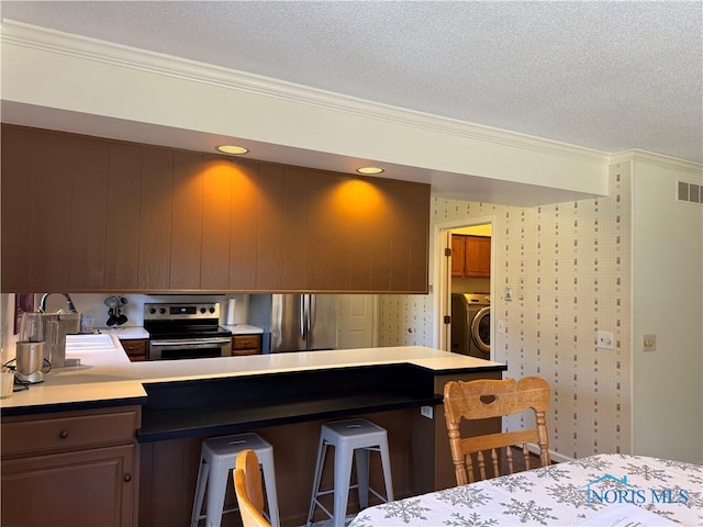 kitchen with washer / dryer, a textured ceiling, appliances with stainless steel finishes, and wallpapered walls