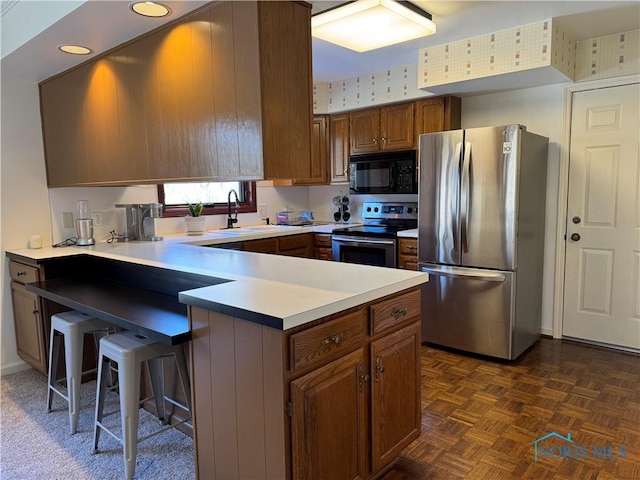 kitchen featuring a breakfast bar area, stainless steel appliances, a peninsula, a sink, and brown cabinets