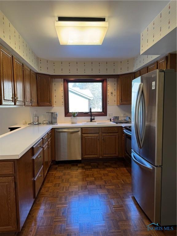 kitchen featuring stainless steel appliances, light countertops, a sink, and wallpapered walls