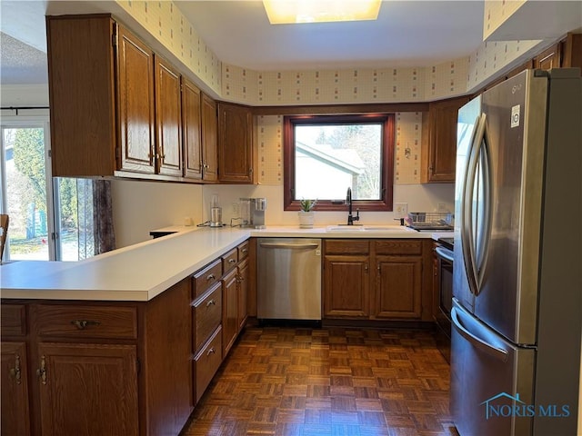 kitchen featuring brown cabinetry, stainless steel appliances, a sink, and light countertops