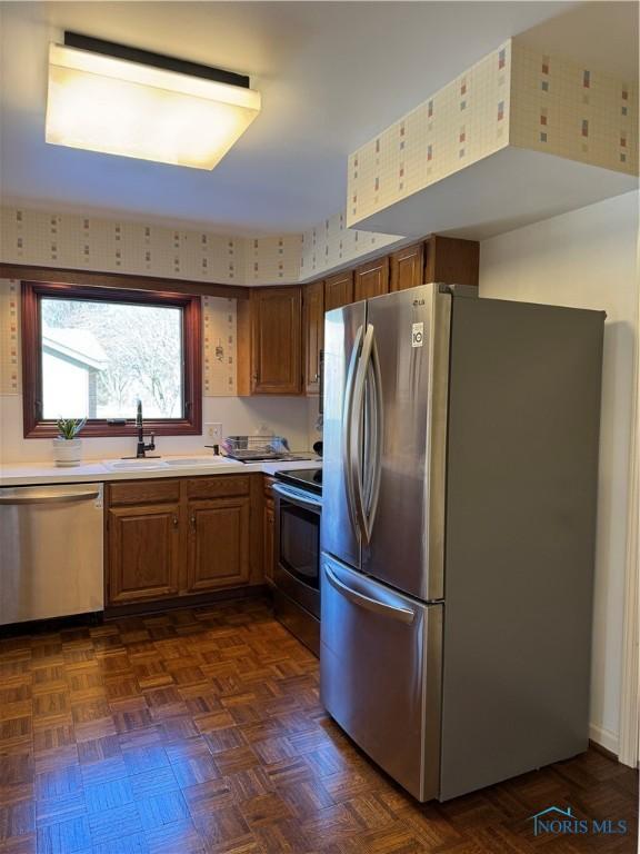 kitchen featuring light countertops, appliances with stainless steel finishes, a sink, and brown cabinets