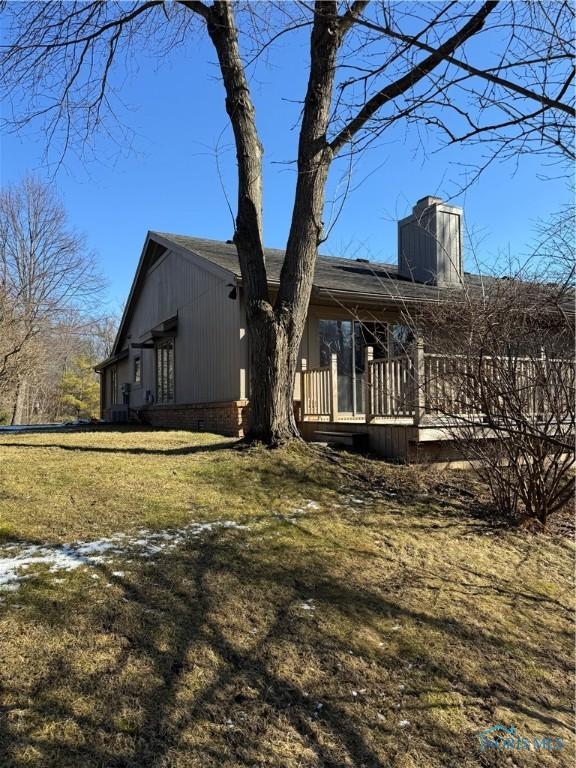 view of side of home featuring a deck, a lawn, and a chimney