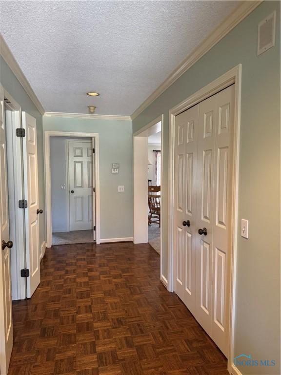 corridor featuring crown molding, visible vents, baseboards, and a textured ceiling