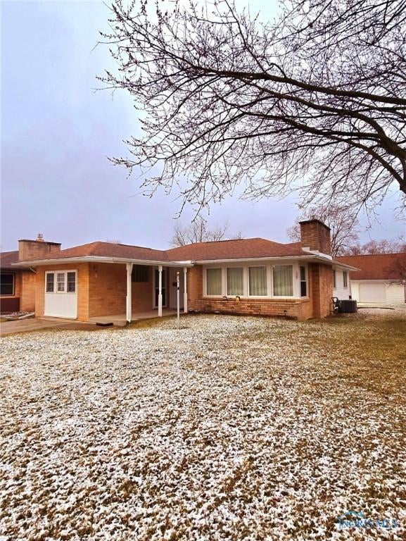 single story home featuring central air condition unit, brick siding, and a chimney