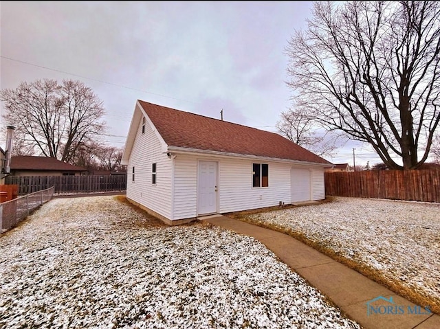 rear view of house featuring an outdoor structure, fence, a detached garage, and a shingled roof