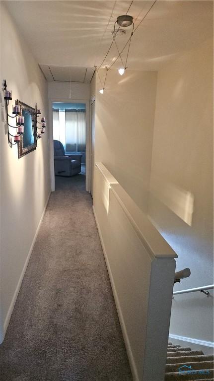 hallway featuring attic access, carpet flooring, and baseboards