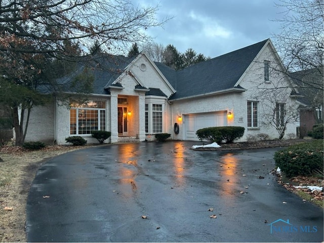 view of front facade featuring an attached garage, a shingled roof, and aphalt driveway