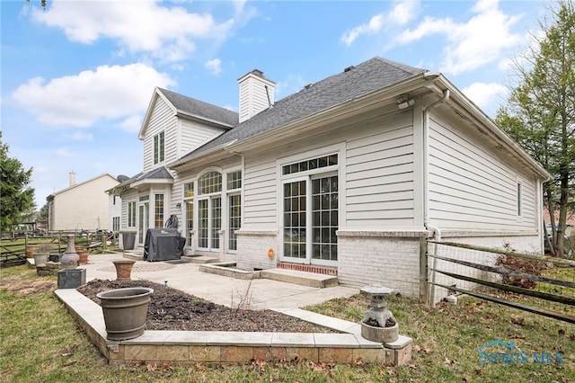 back of property featuring a patio area, a chimney, fence, brick siding, and a shingled roof