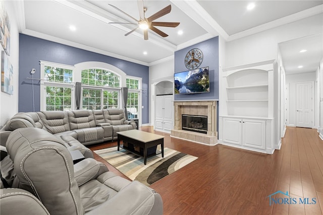 living area with crown molding, ceiling fan, wood finished floors, a fireplace, and built in features