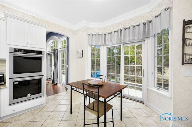 dining room with light tile patterned flooring, ornamental molding, baseboards, and arched walkways
